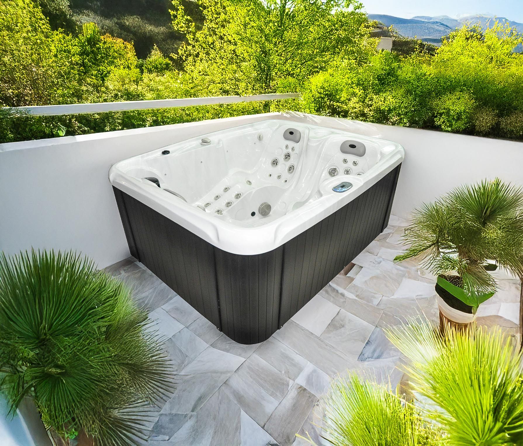 Un spa rectangulaire sur un patio carrelé avec des plantes vertes et un mur blanc, entouré d'une verdure luxuriante.