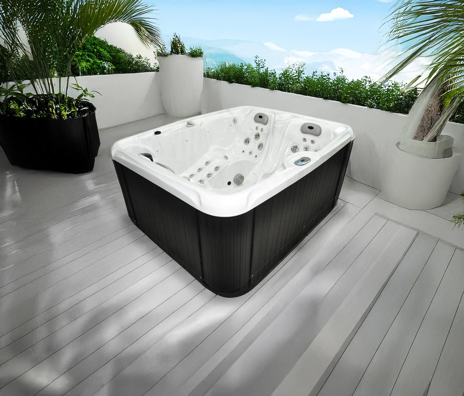 Un jacuzzi sur une terrasse blanche, entouré de verdure et offrant une vue panoramique sur les montagnes. Le jacuzzi est noir et blanc.