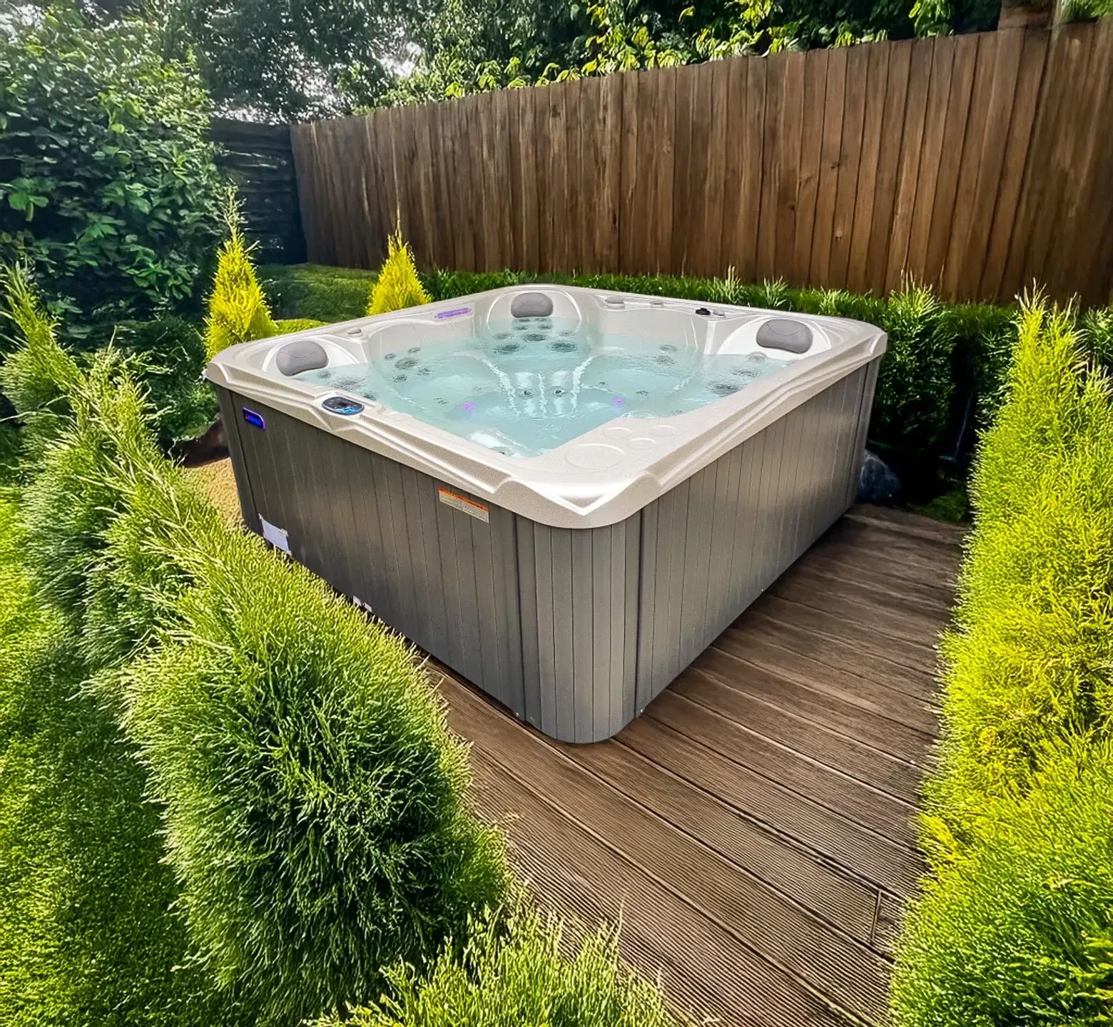 Un spa se trouve sur une terrasse en bois, entourée d'arbustes verts et d'une clôture en bois.