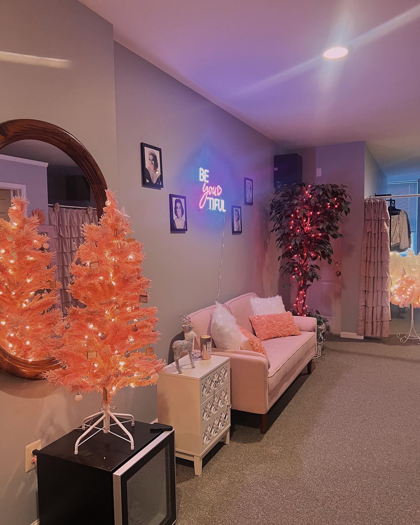 A room with a pink sofa, orange trees, a mirrored wall, and neon sign.