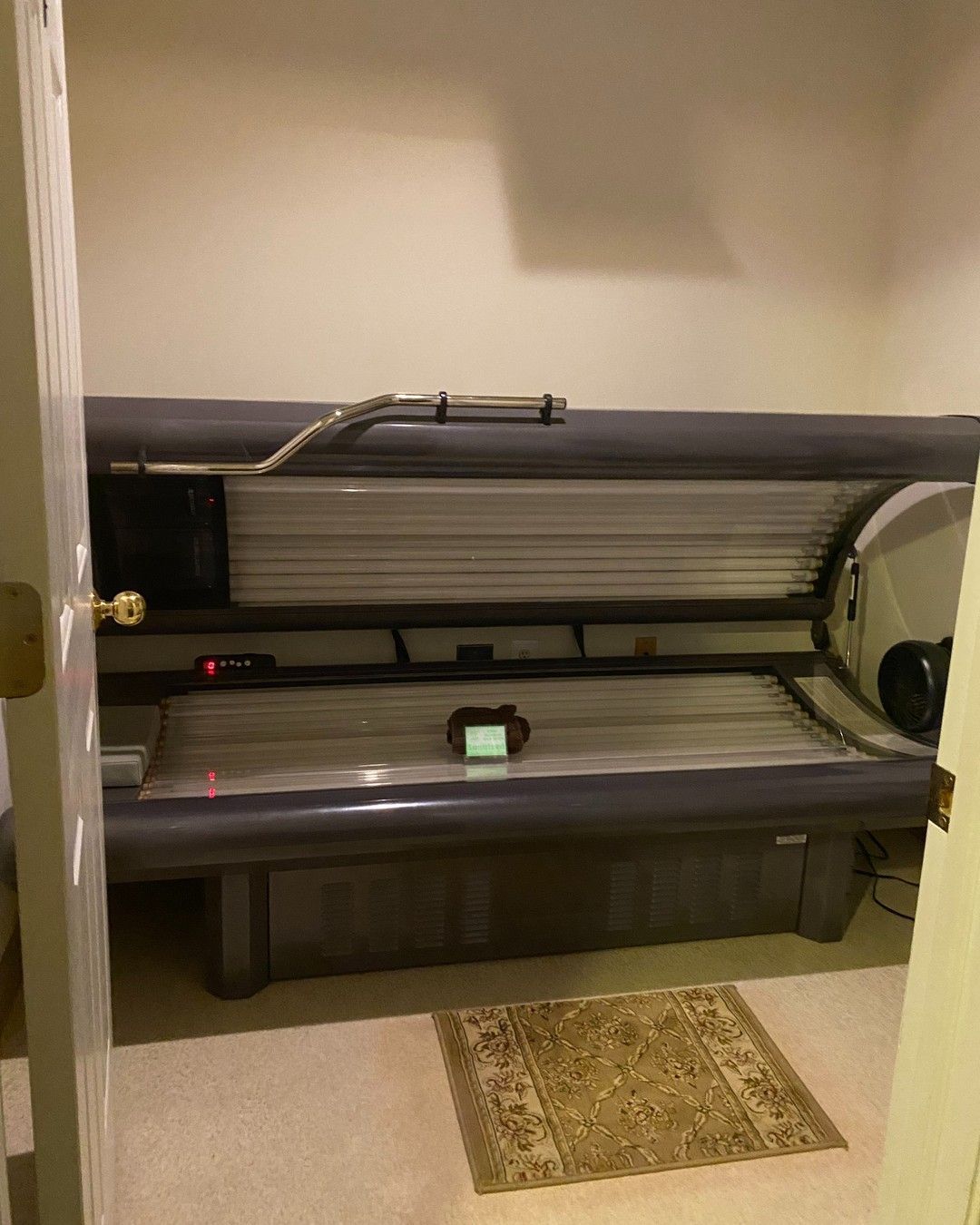 Tanning bed in a beige-walled room, with a rug at the foot.