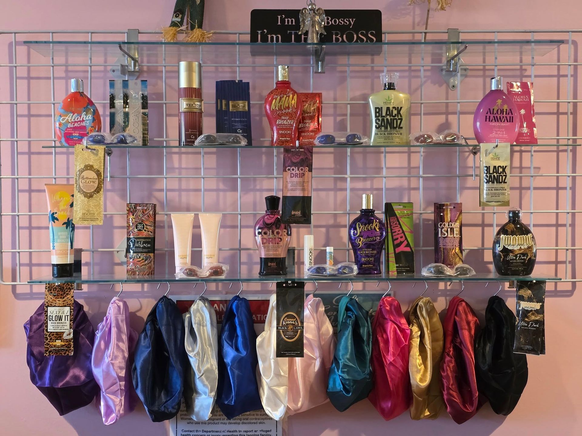 Shelves with beauty products, including perfumes and lotions, above silk bonnets. Pink wall backdrop.