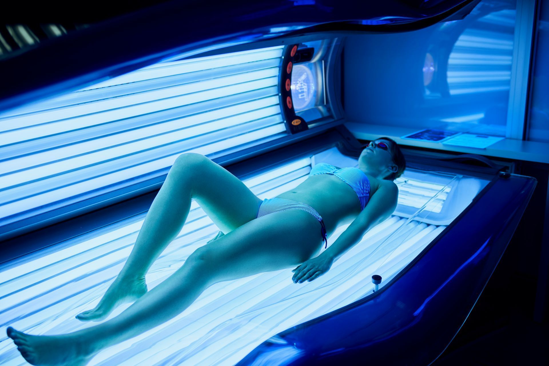 Woman lying in a tanning bed, exposed to blue UV light.