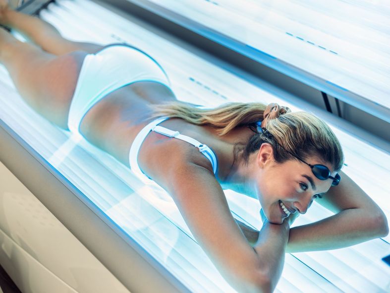 Woman in a tanning bed, wearing goggles and a bikini, smiling.