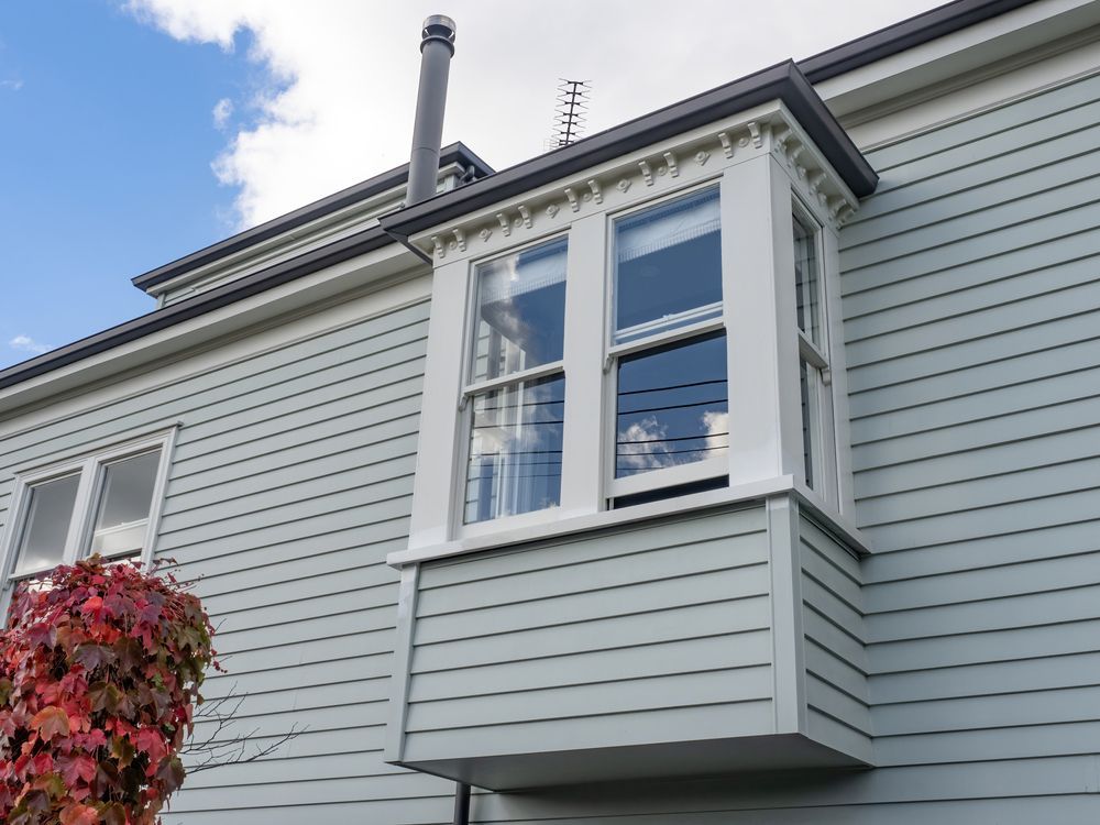 Light blue house exterior featuring a bay window with white trim and decorative brackets under the roofline — Working Windows in Ocean Shores, NSW