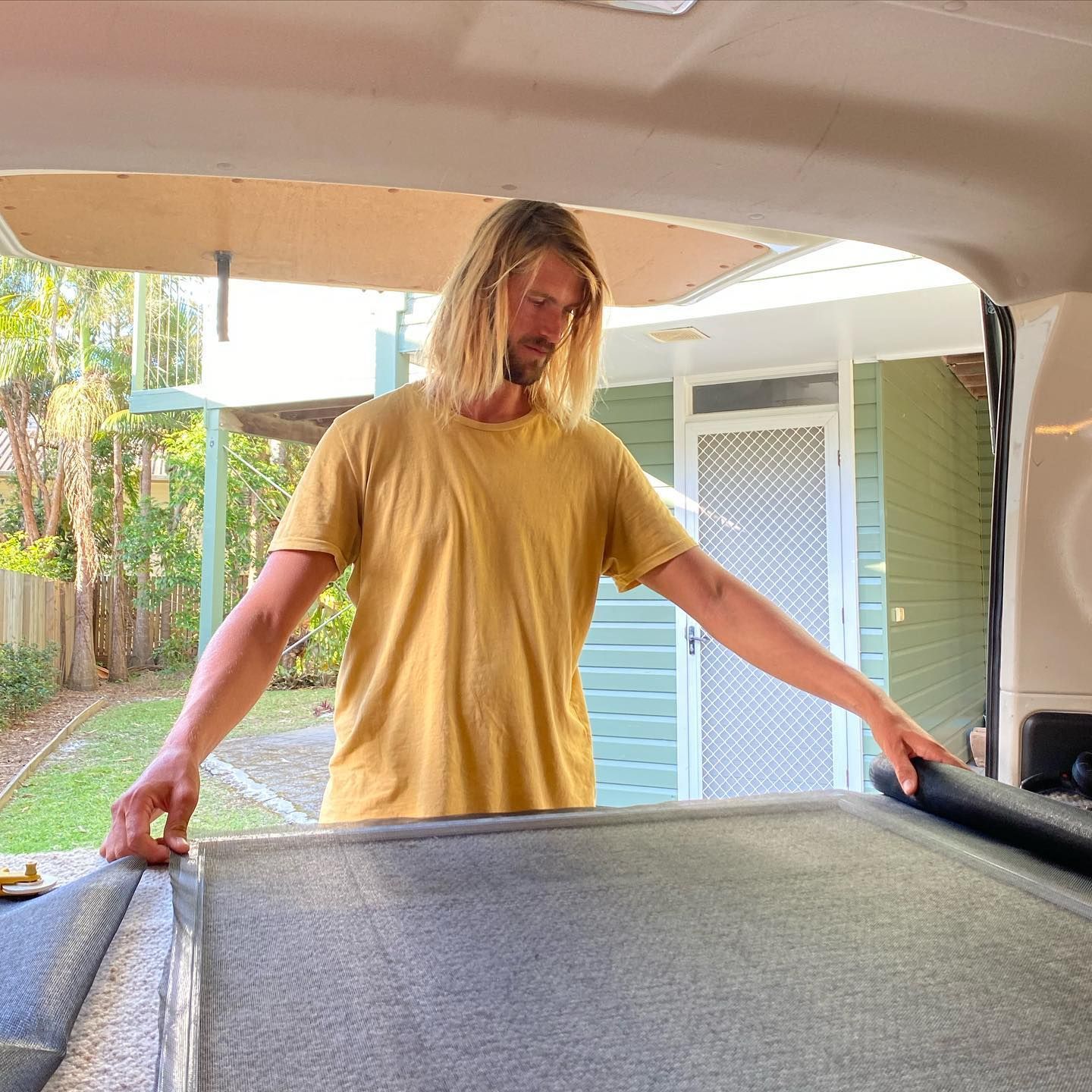 Man with long blond hair working on a van interior, wearing a yellow shirt, outdoors — Working Windows in Byron Bay, NSW