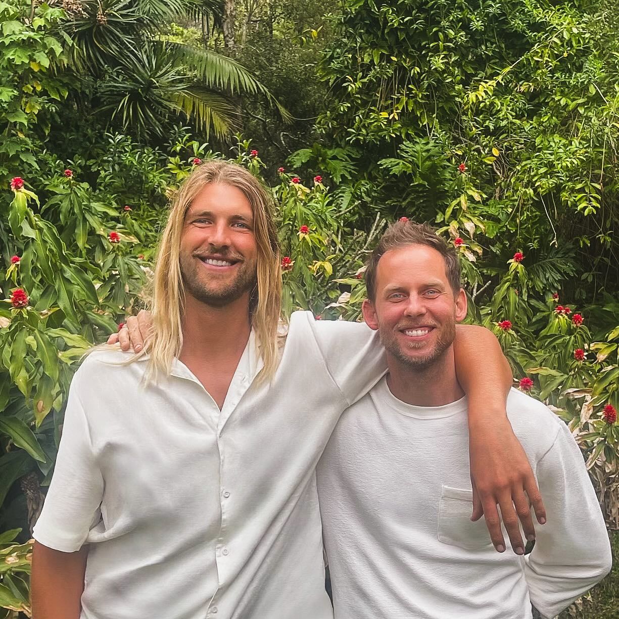 Two smiling men stand shoulder-to-shoulder in front of lush green foliage — Working Windows in Byron Bay, NSW