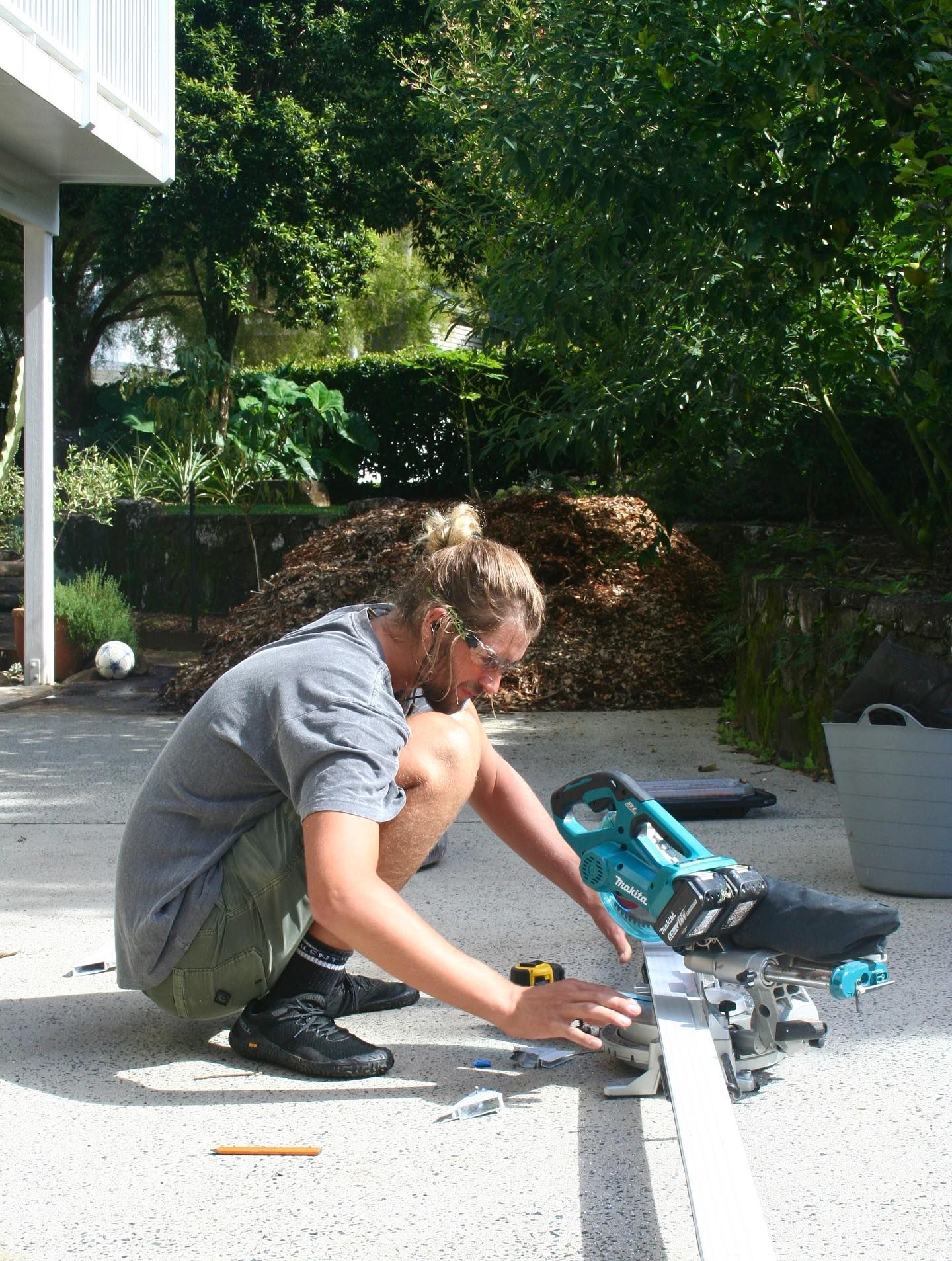 Man Using a Miter Saw Outdoors to Cut a White Board on a Concrete Surface — Working Windows in Byron Bay, NSW