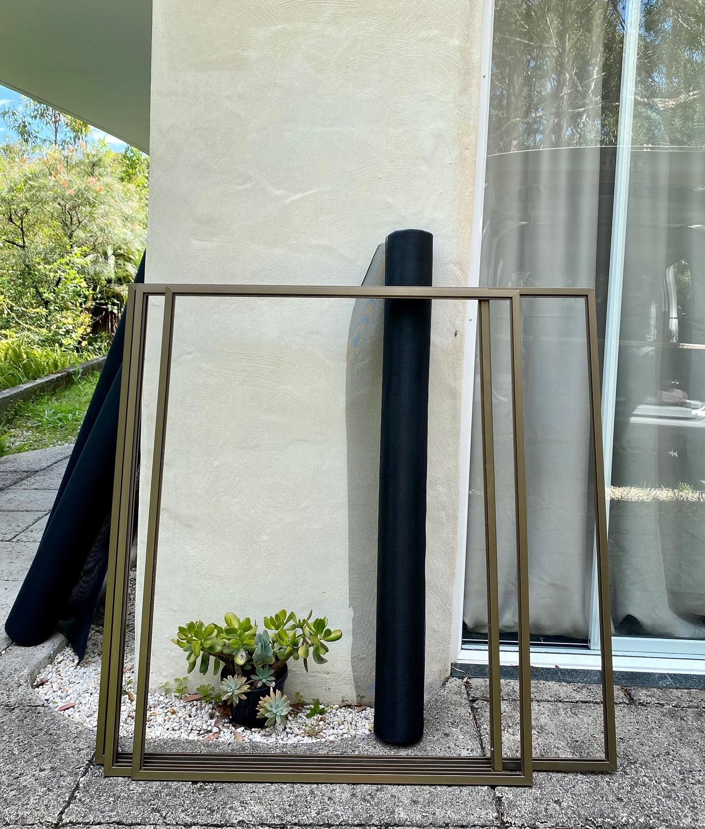 Two Metal Frames, a Roll of Black Material, and a Plant Sit on a Patio — Working Windows in Byron Bay, NSW
