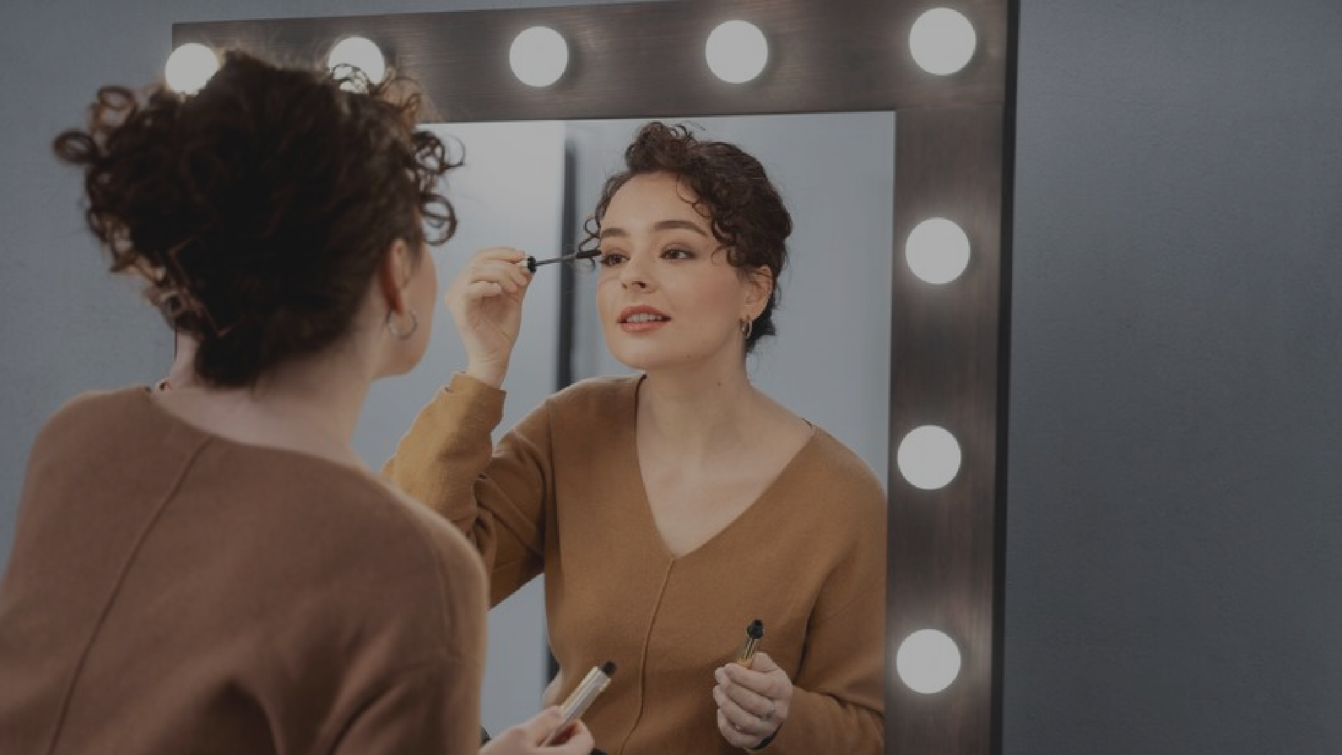 Una mujer se aplica rímel en las pestañas frente a un espejo.