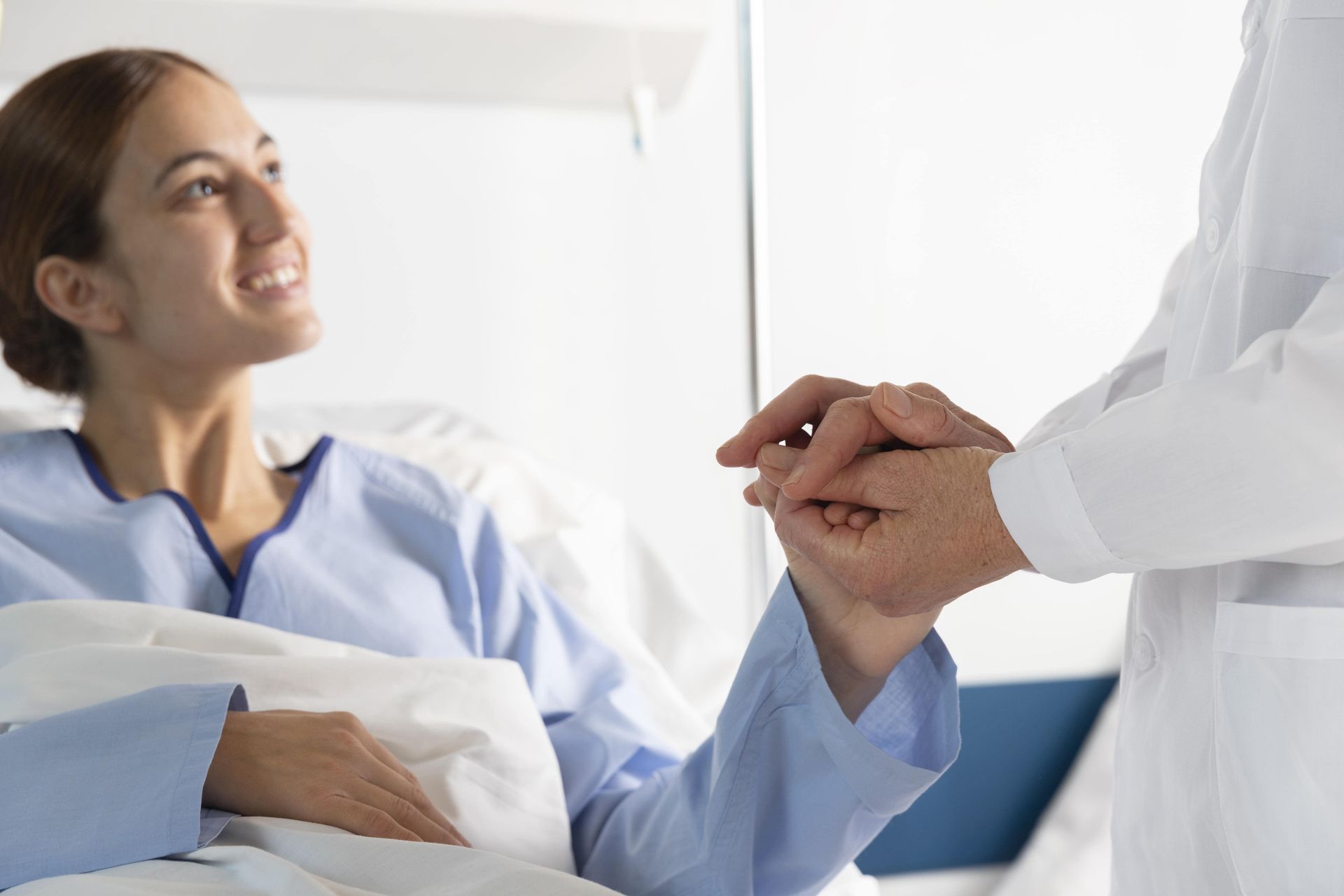 Un médico sostiene la mano de un paciente en una cama de hospital.