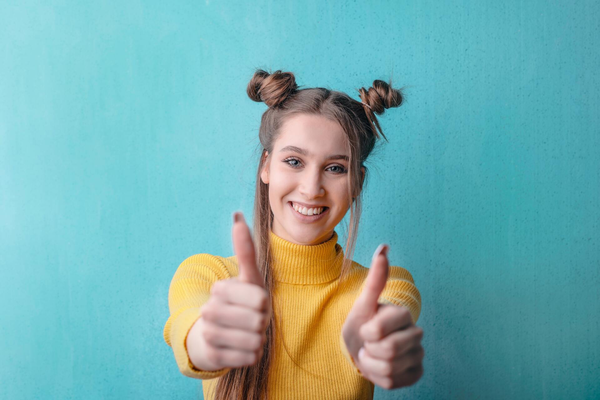 Una mujer joven con un suéter amarillo está haciendo dos pulgares hacia arriba.
