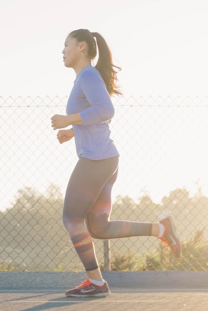 Una mujer corre por una acera junto a una valla de alambre.