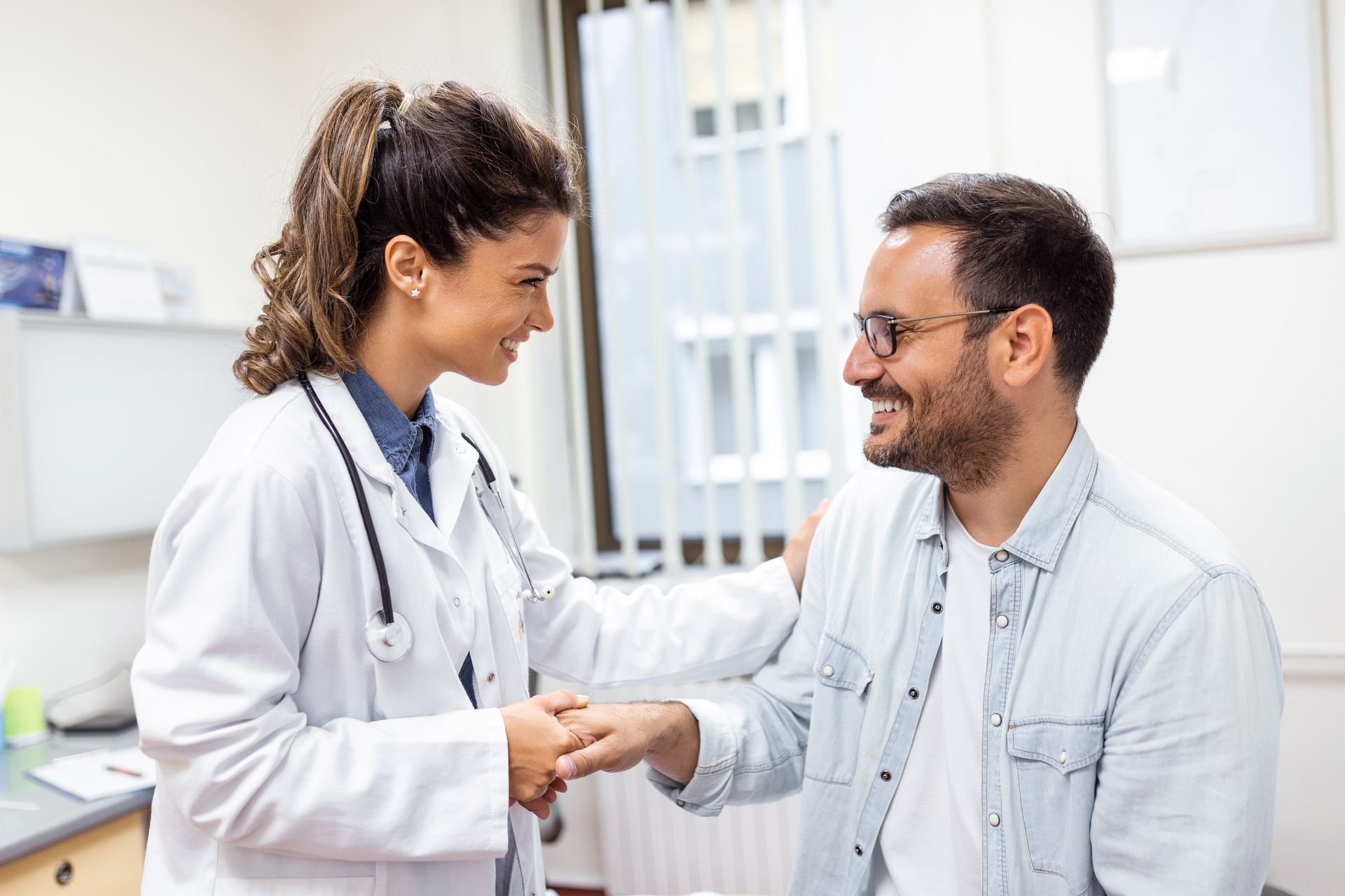 Un médico sostiene la mano de un paciente en una cama de hospital.