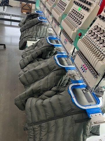 Row of embroidery machines embroidering gray puffer jackets.
