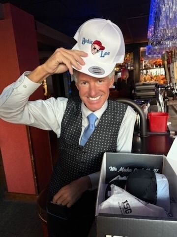 Man in vest holds up a white trucker hat with logo 