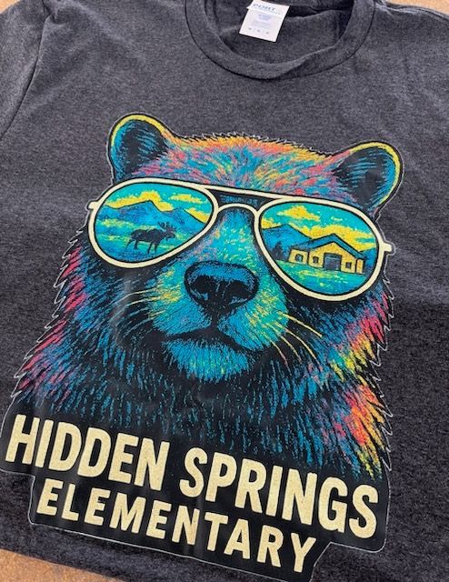 Bear wearing sunglasses with a reflection of a house and mountains. Text: Hidden Springs Elementary.
