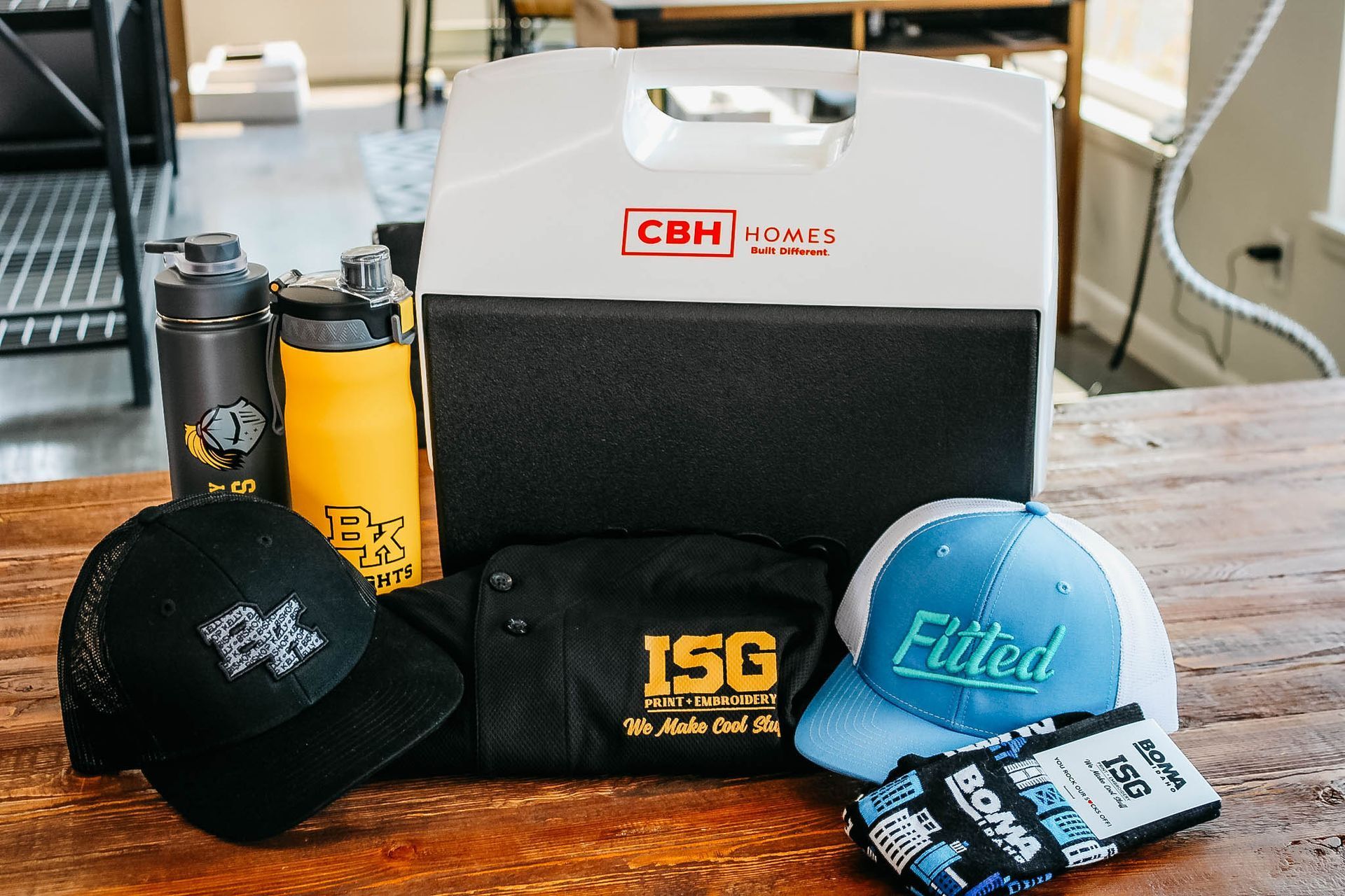 Promotional items: hats, water bottles, cooler, shirt, and wristbands with company logos on a table.
