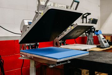 Heat press machine with open black top and blue bottom, in a workshop.