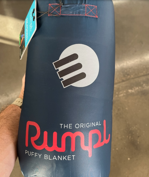A rolled-up navy Rumpl puffy blanket with the brand's logo and text.