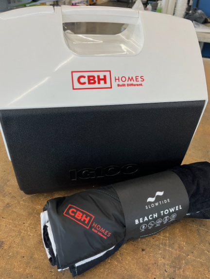 White and black Igloo cooler and rolled-up beach towel with CBH Homes logo.