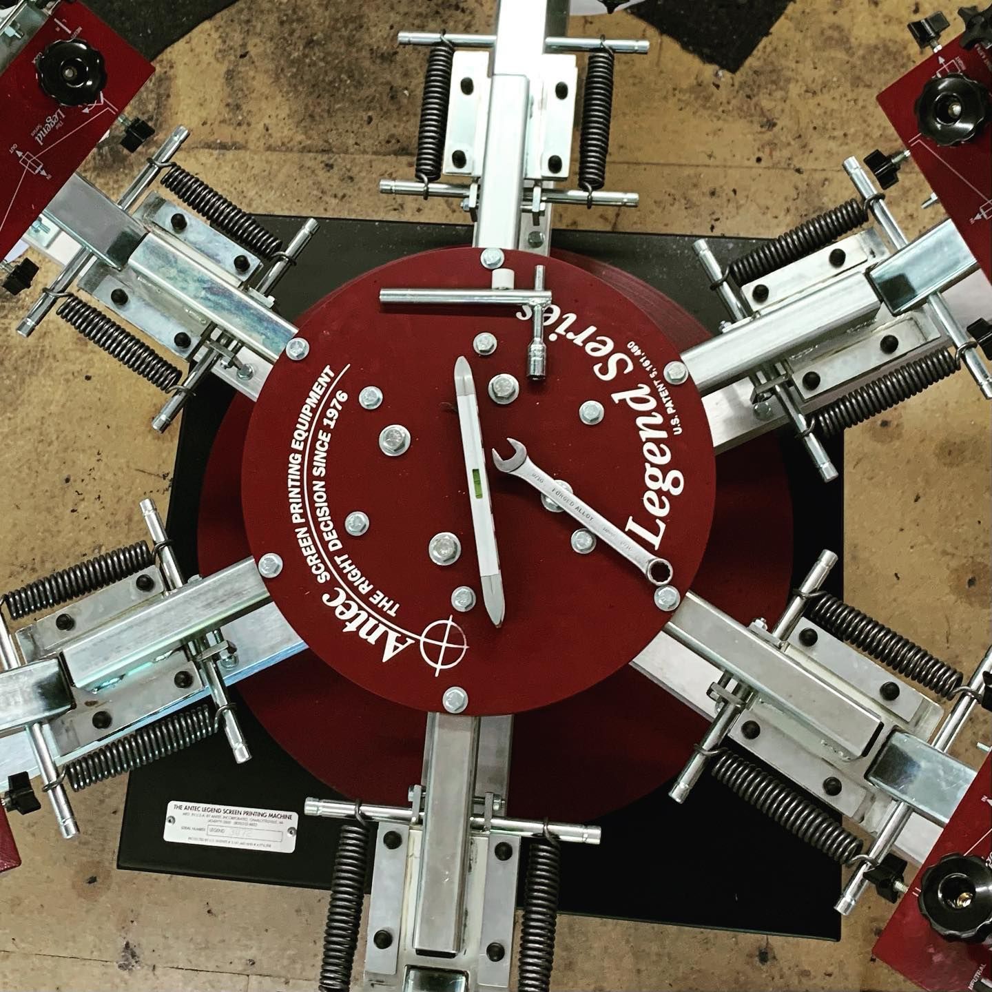 Overhead view of a red and silver screen printing machine with tools resting on it.