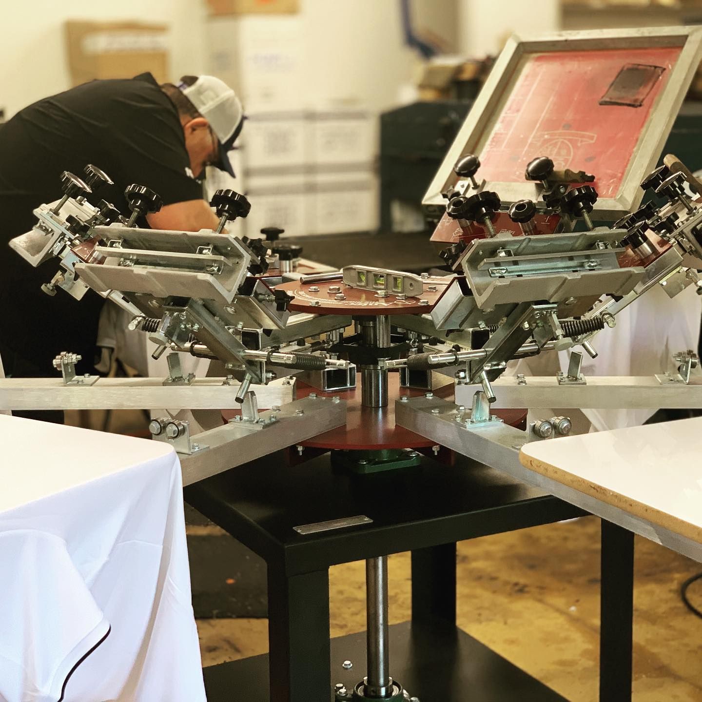 Person setting up screen printing machine with a white shirt on the table.