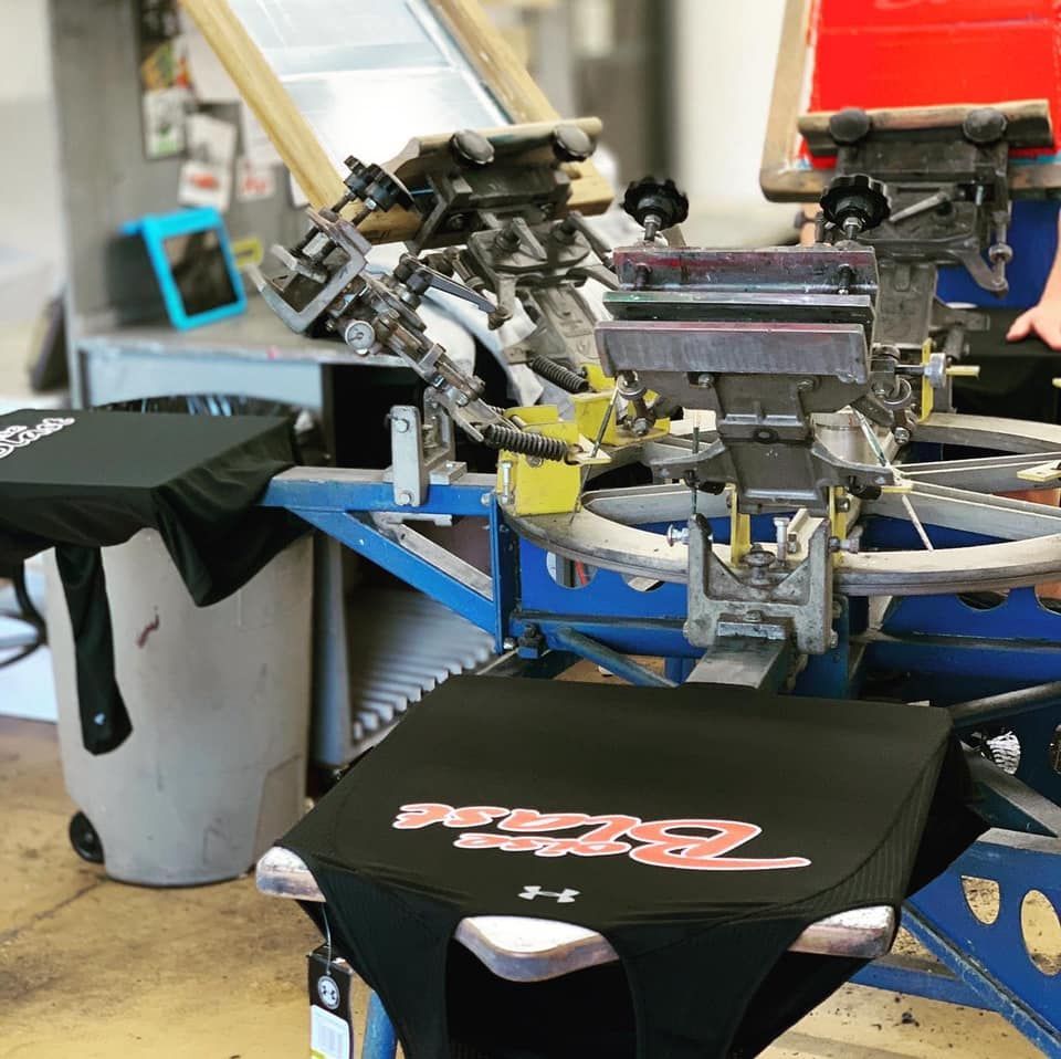Screen printing machine printing red and white design on black t-shirt.