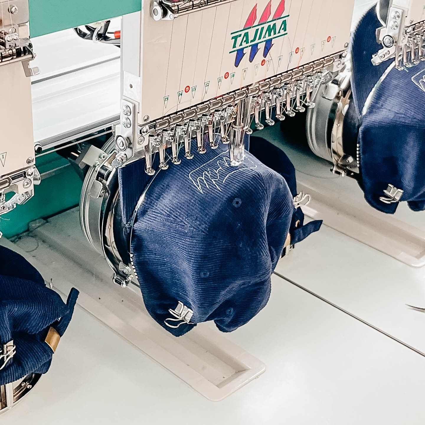Embroidery machine stitching designs onto blue baseball caps.