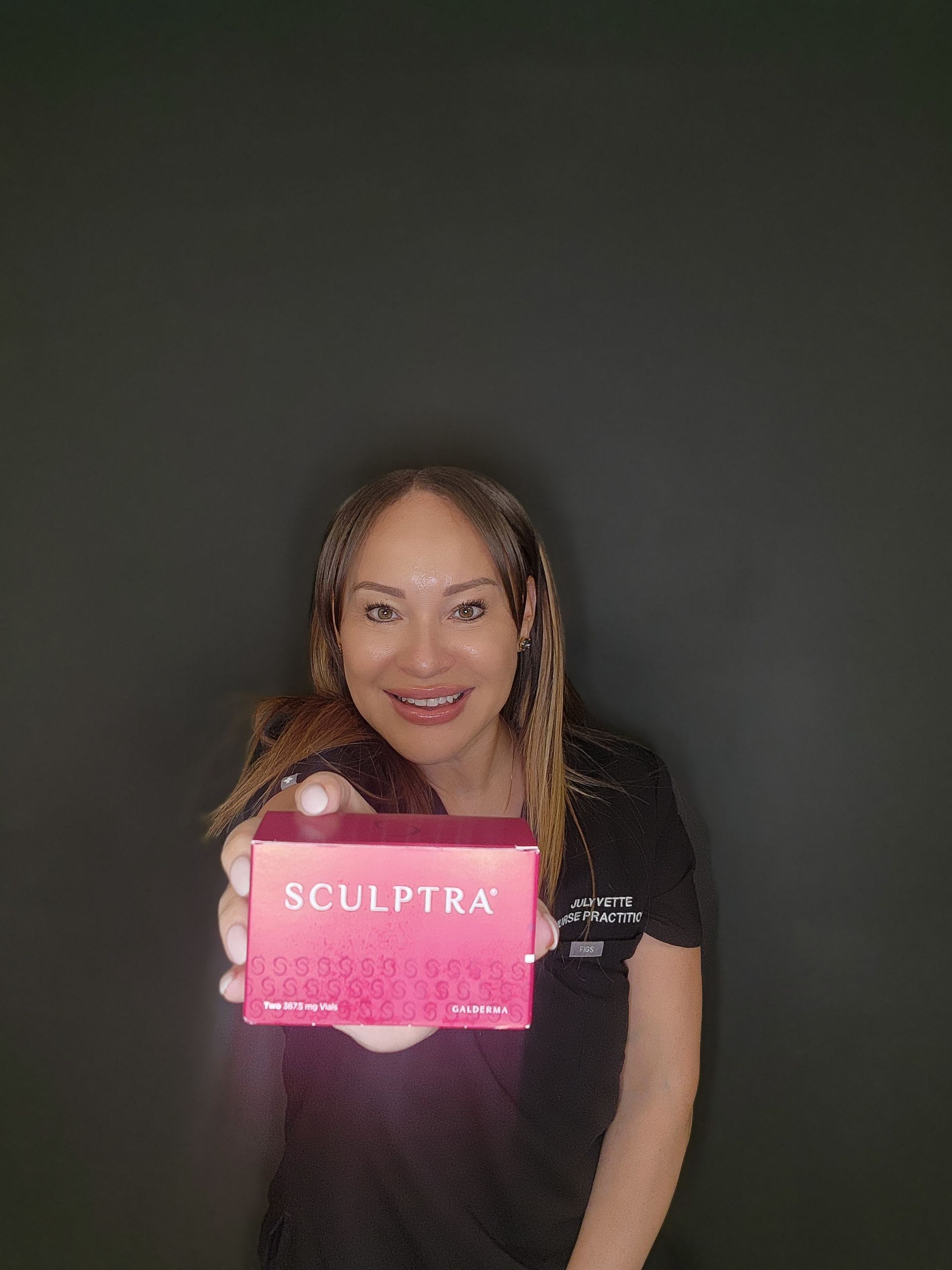 Woman holding a Sculptra box, smiling at the camera, against a dark background.