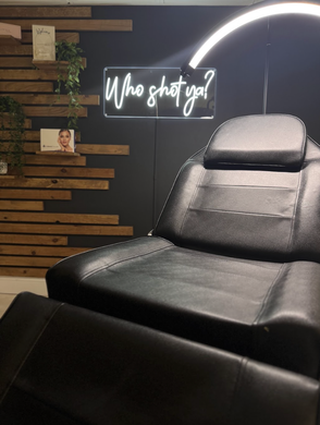 A black chair is in a room with a neon sign on the wall.