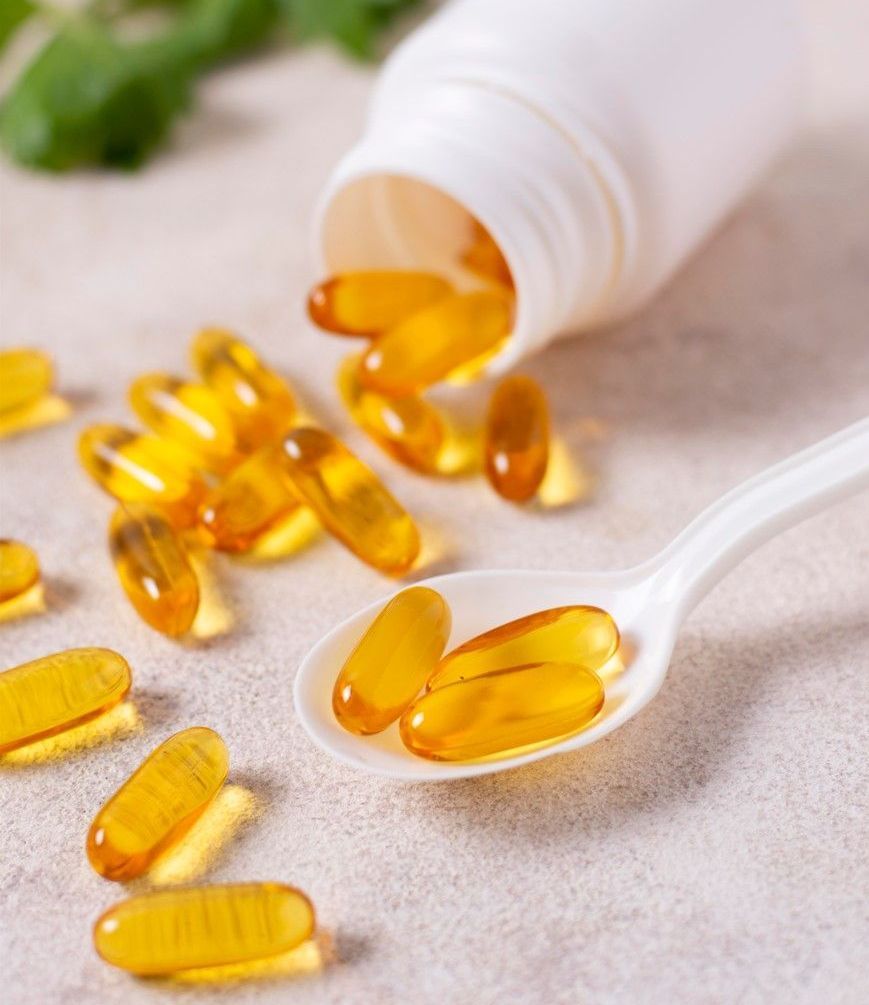 A spoon filled with yellow capsules next to a bottle