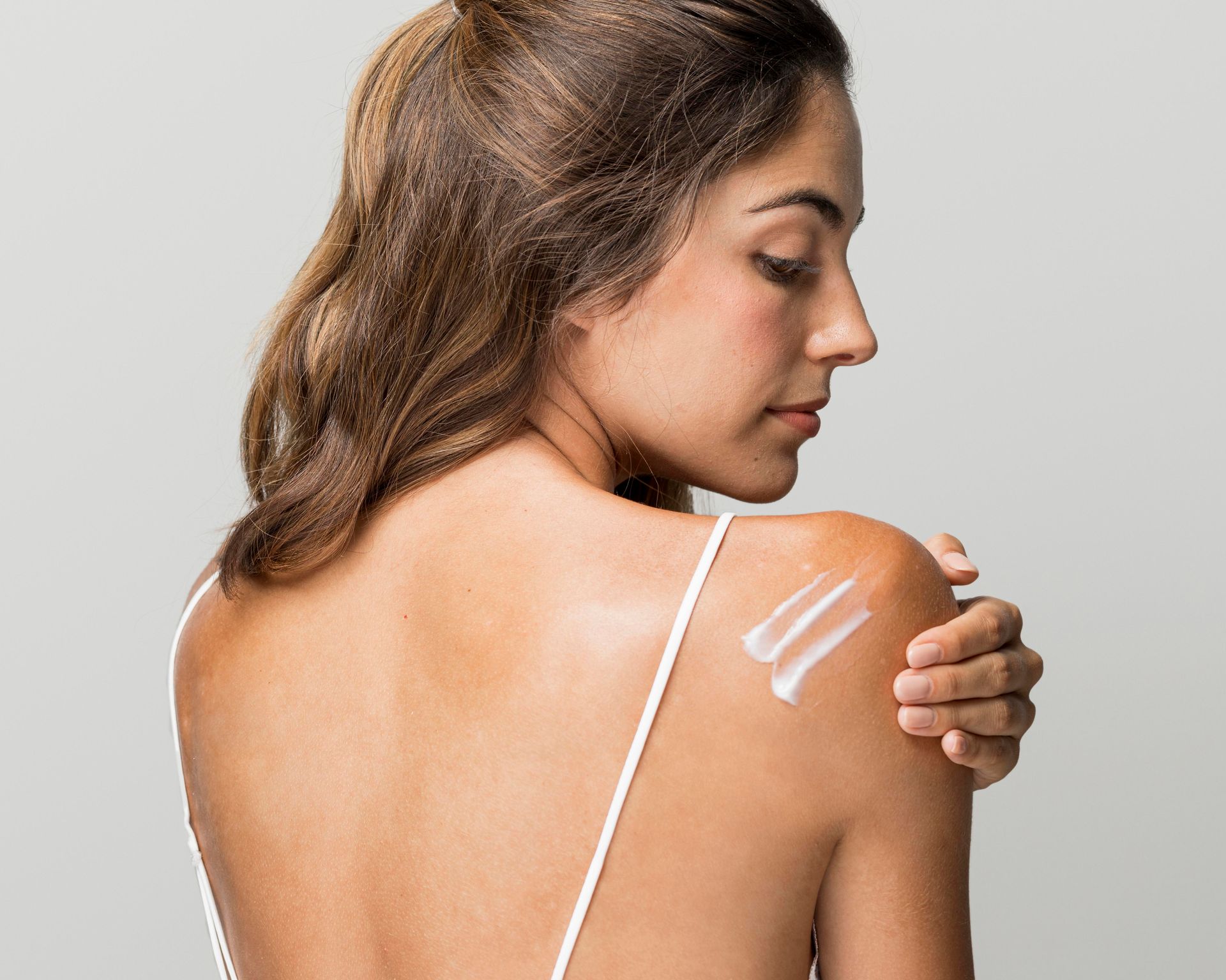 A woman is applying lotion to her shoulder.