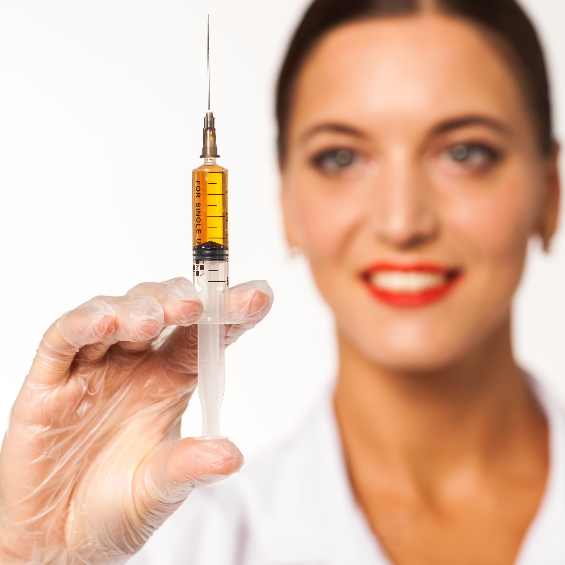 A woman is holding a syringe with a yellow liquid in it