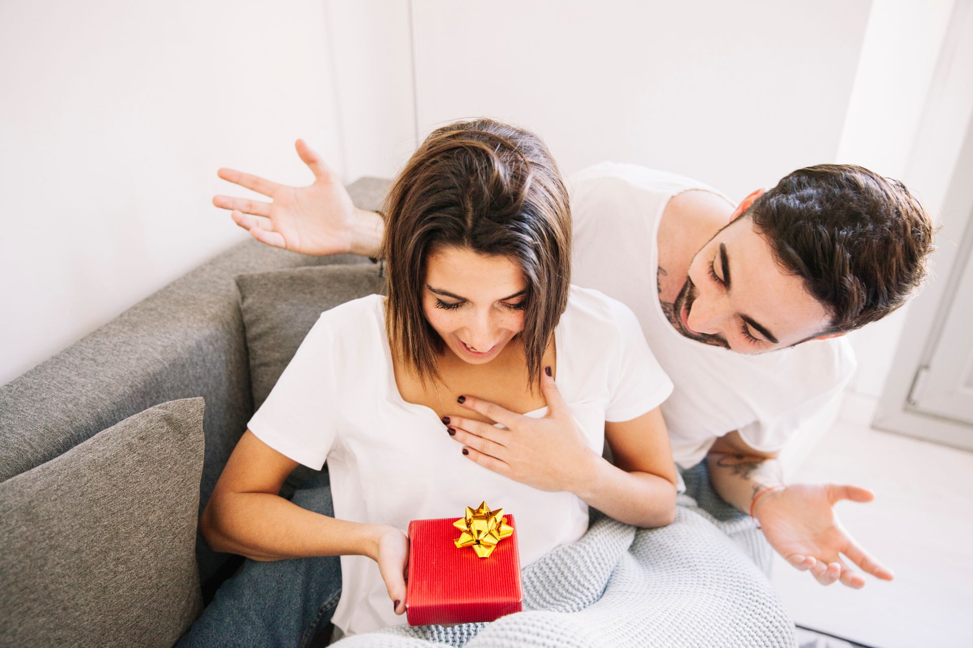 A man is giving a gift to a woman who is sitting on a couch.