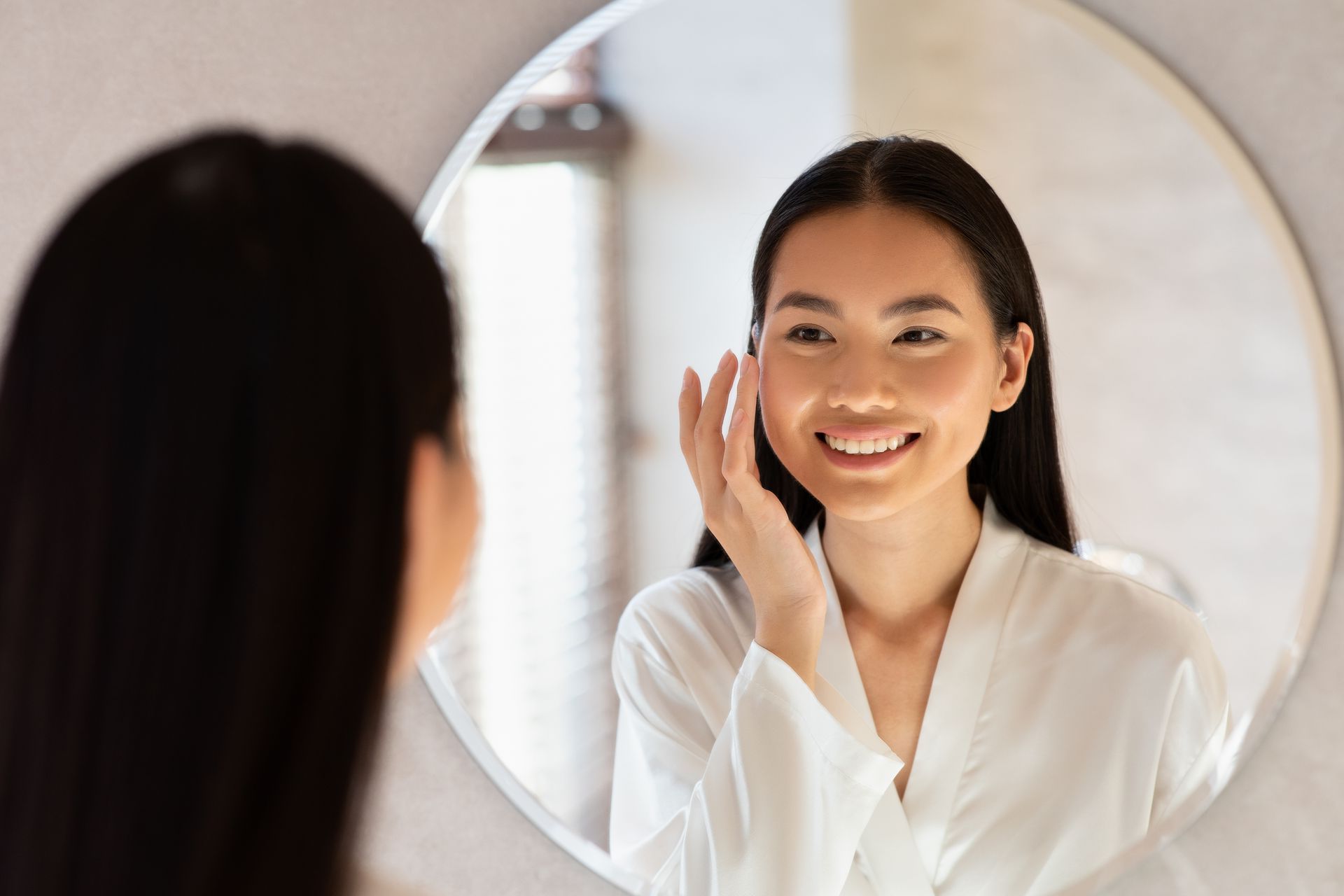 A woman is looking at her face in a mirror.