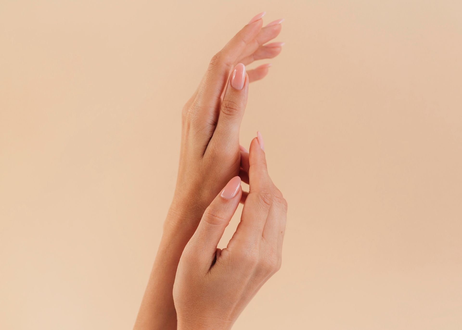 Two hands gently touching, centered against a solid beige background, featuring neatly manicured nails.