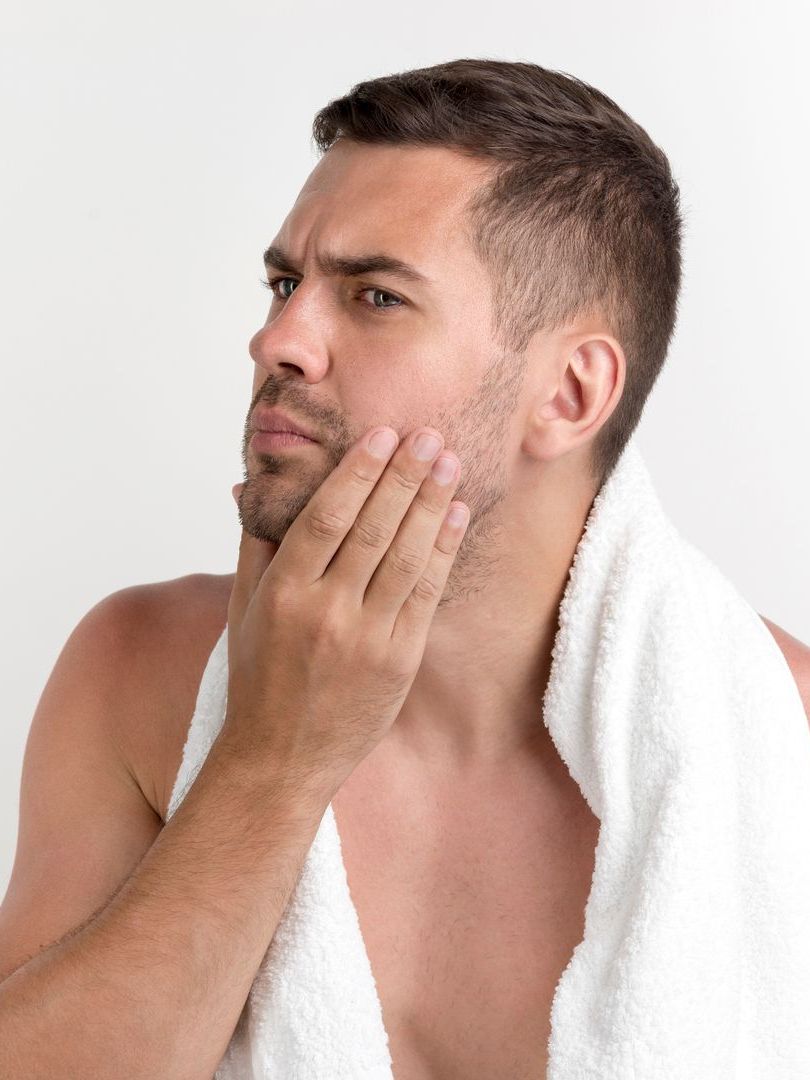 Man with a towel around his neck, examining his face, possibly after shaving.