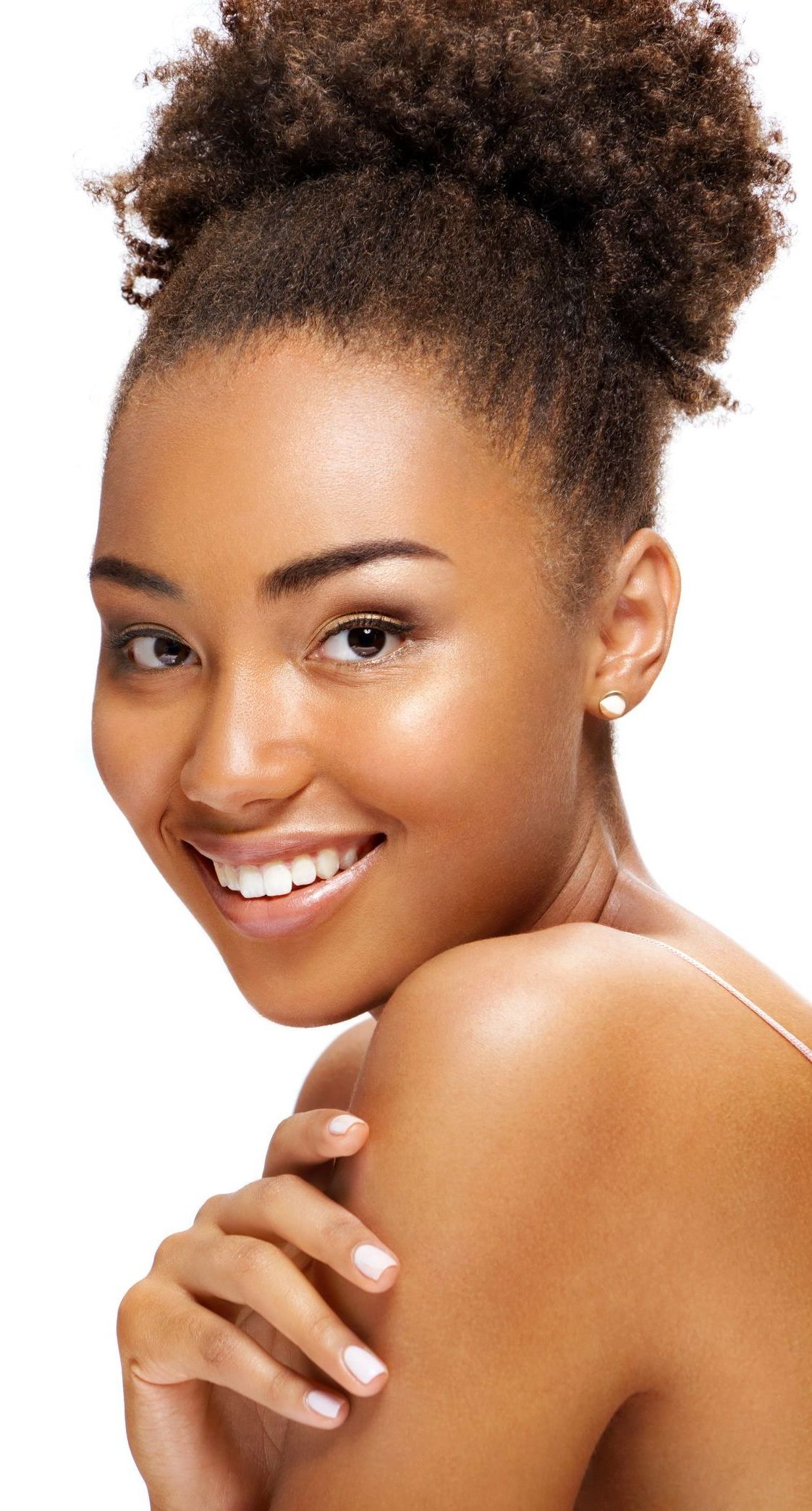 A woman with curly hair is smiling and touching her shoulder.