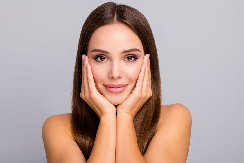 A woman is holding her face with her hands and smiling.