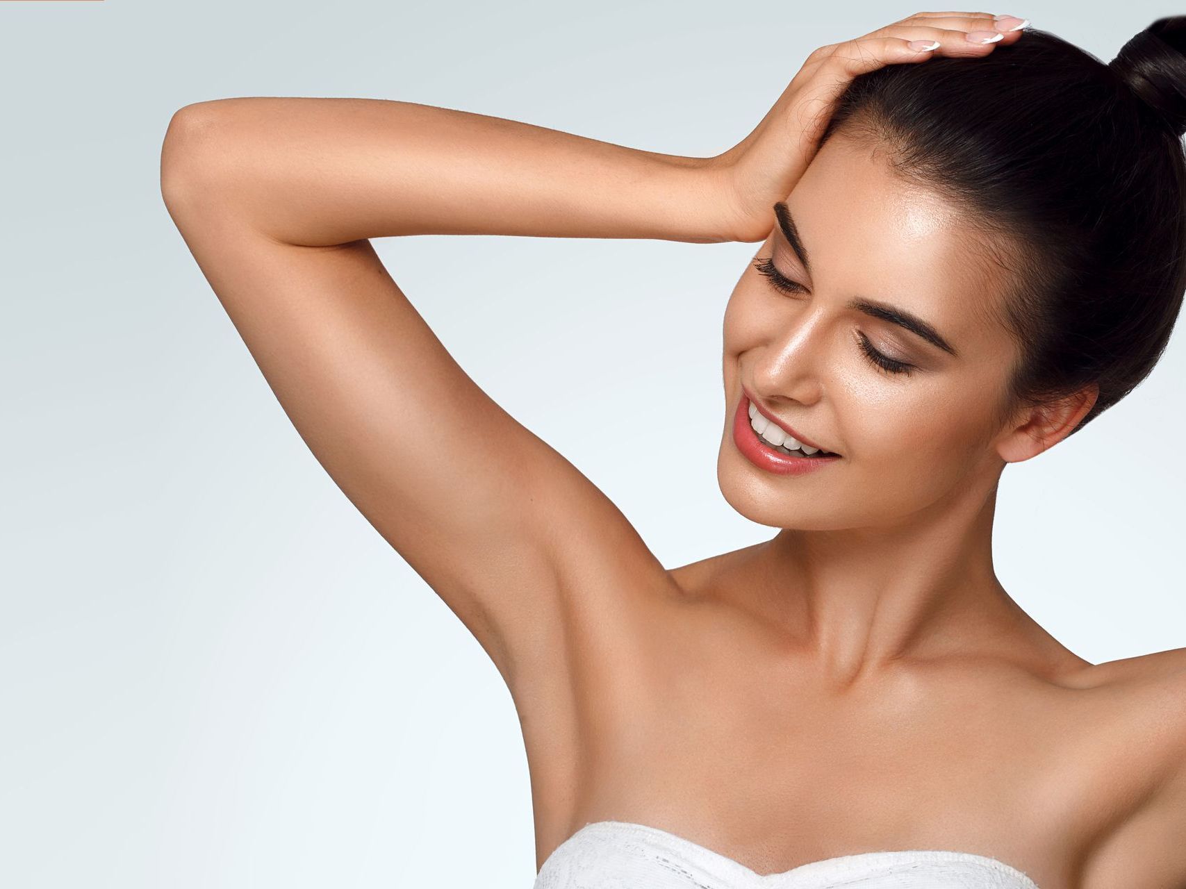 A woman is smiling and holding her hair in a bun.