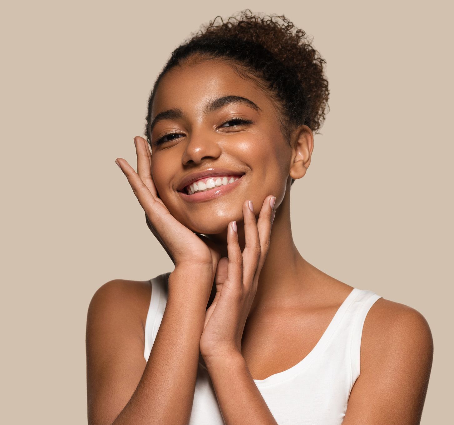 A woman is smiling and touching her face with her hands.