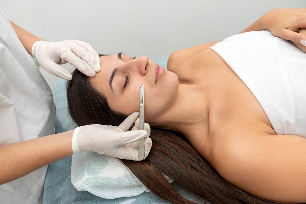 Woman receiving a cosmetic skin procedure; doctor with a scalpel, lying on a table.