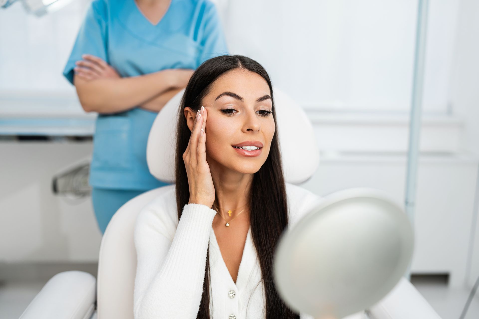 A woman is sitting in a chair looking at her face in a mirror.