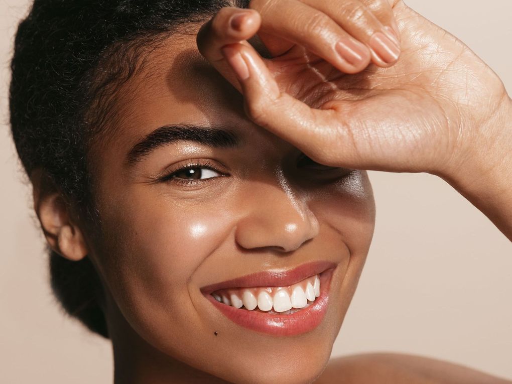 A woman is smiling and covering her face with her hand.