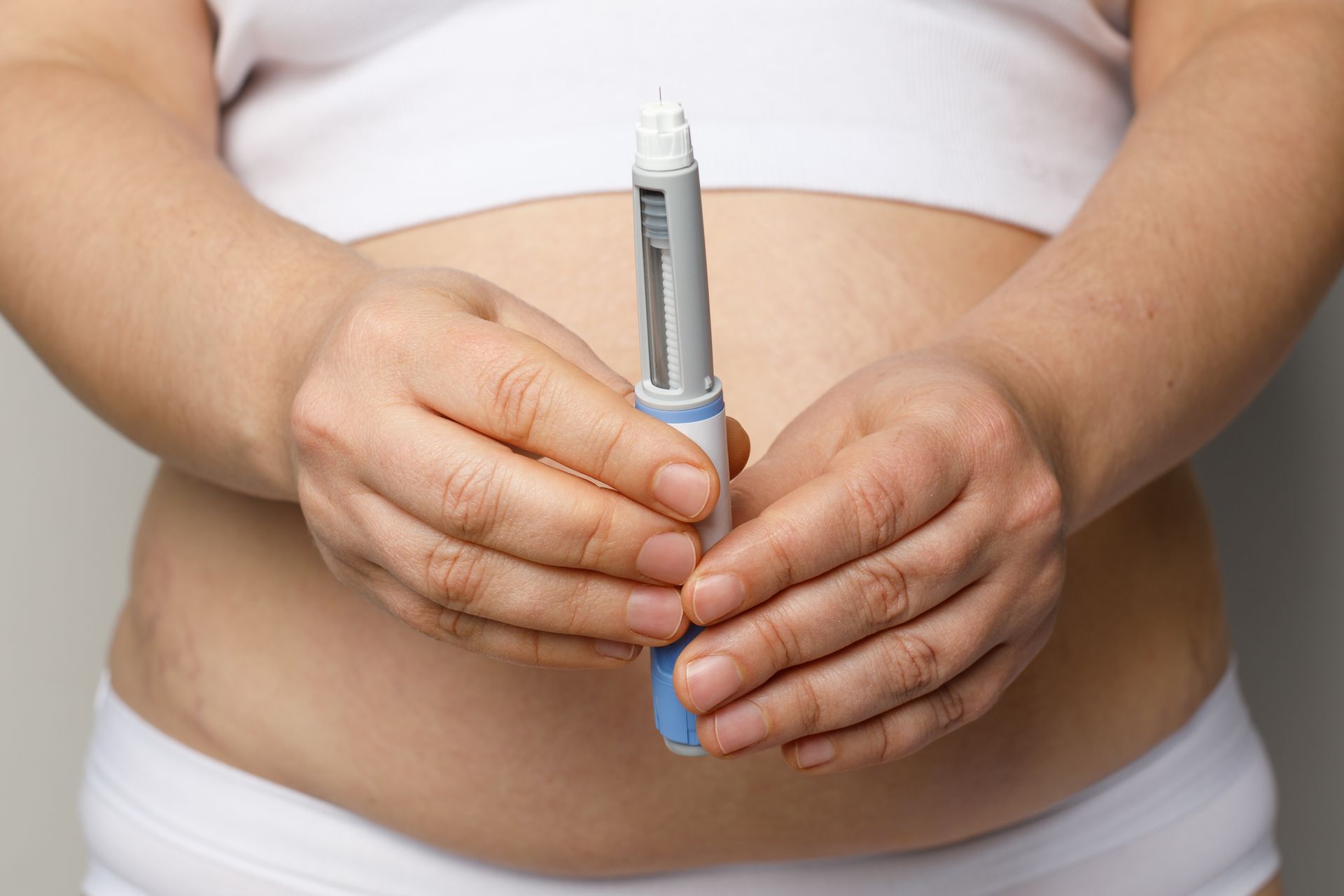 A pregnant woman is holding a pen in front of her belly.