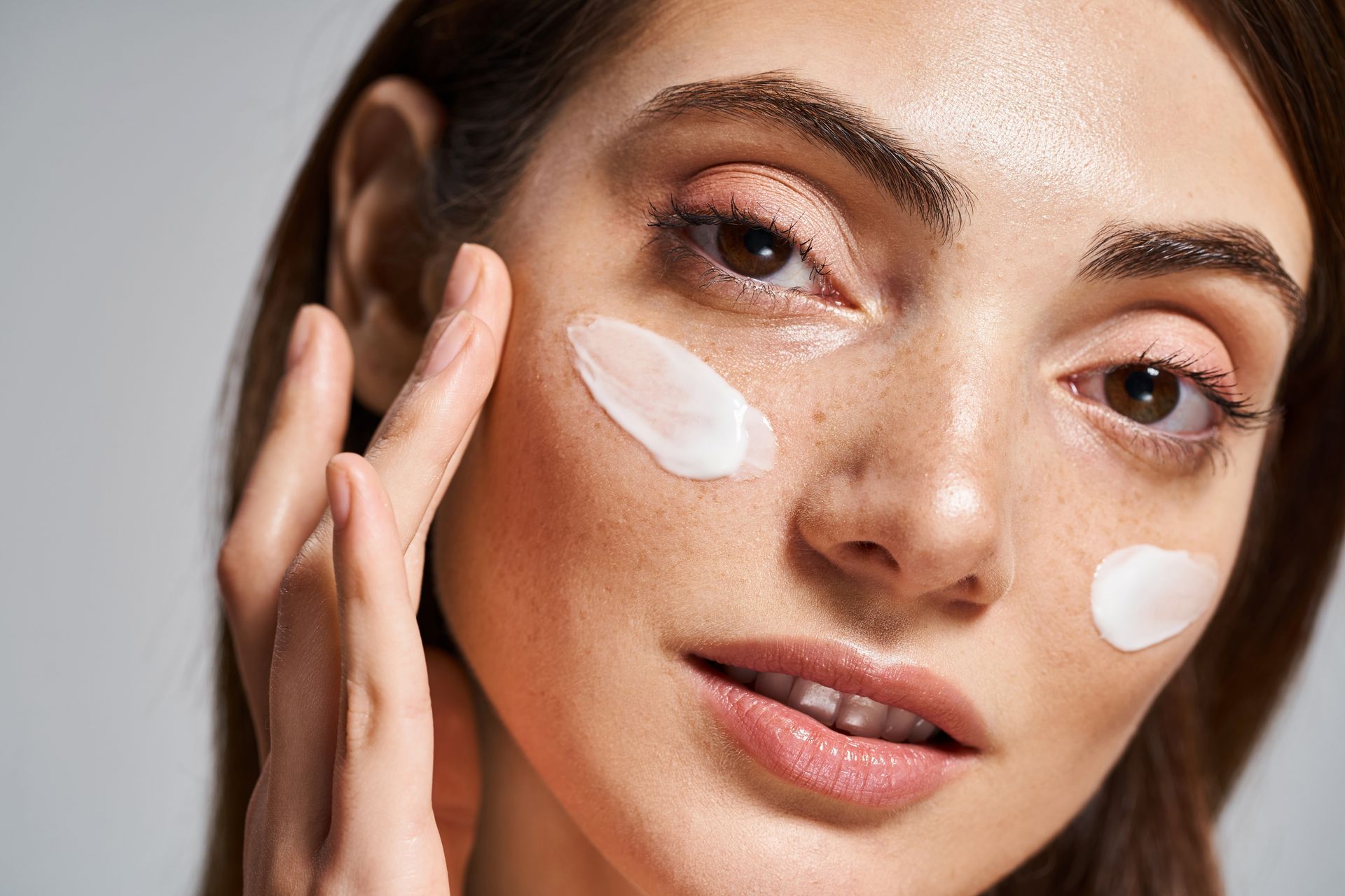 A woman is applying cream to her face.