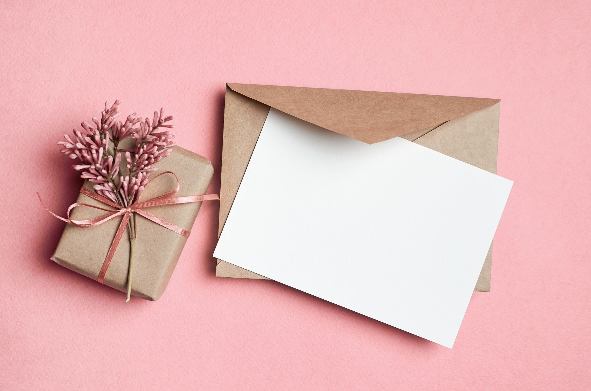 A brown envelope with a card and a gift box on a pink background.