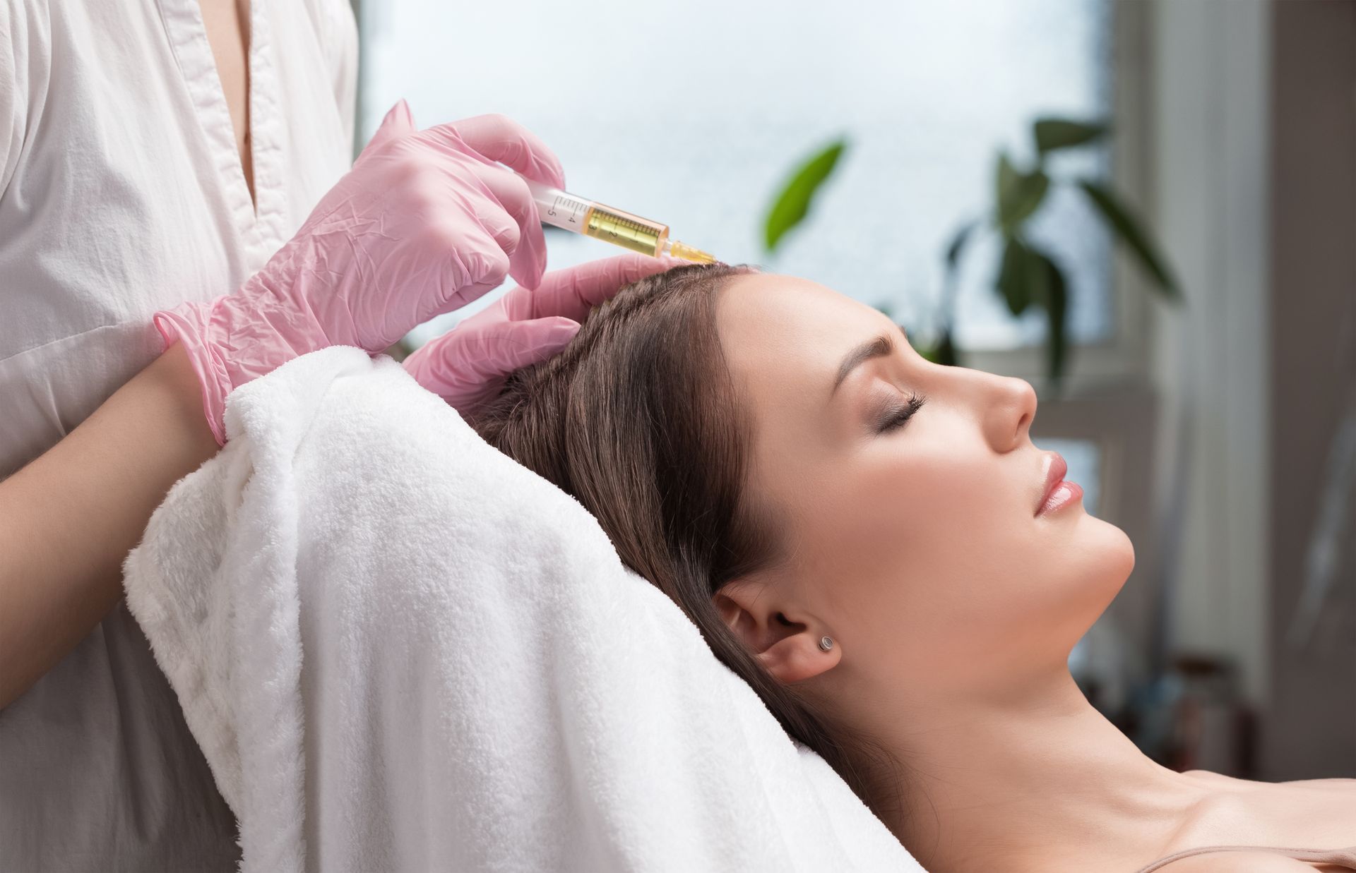 A practitioner in pink gloves administers an injection into a client's scalp during a hair restoration treatment.