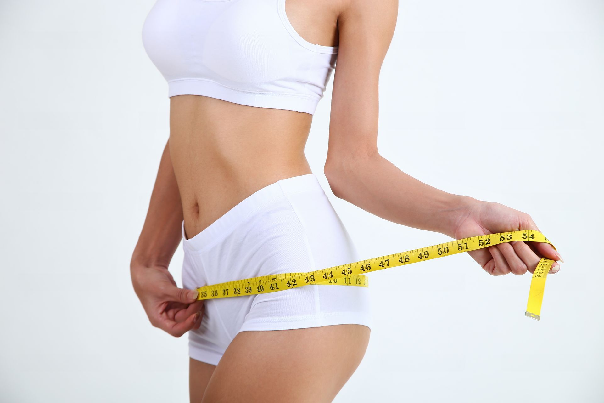 A woman is measuring her waist with a tape measure.